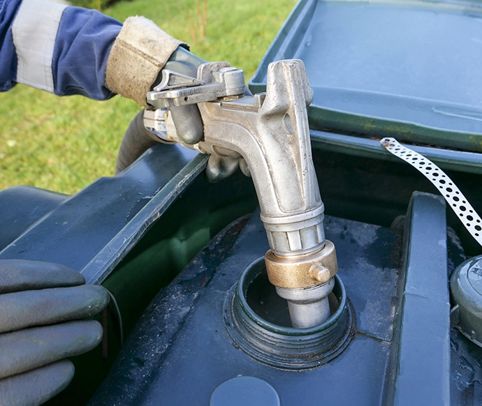 Hand using hose to fill up outdoor home heating oil tank.